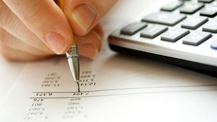 Hand met een potlood die cijfers controleert op een financieel overzicht, naast een rekenmachine
