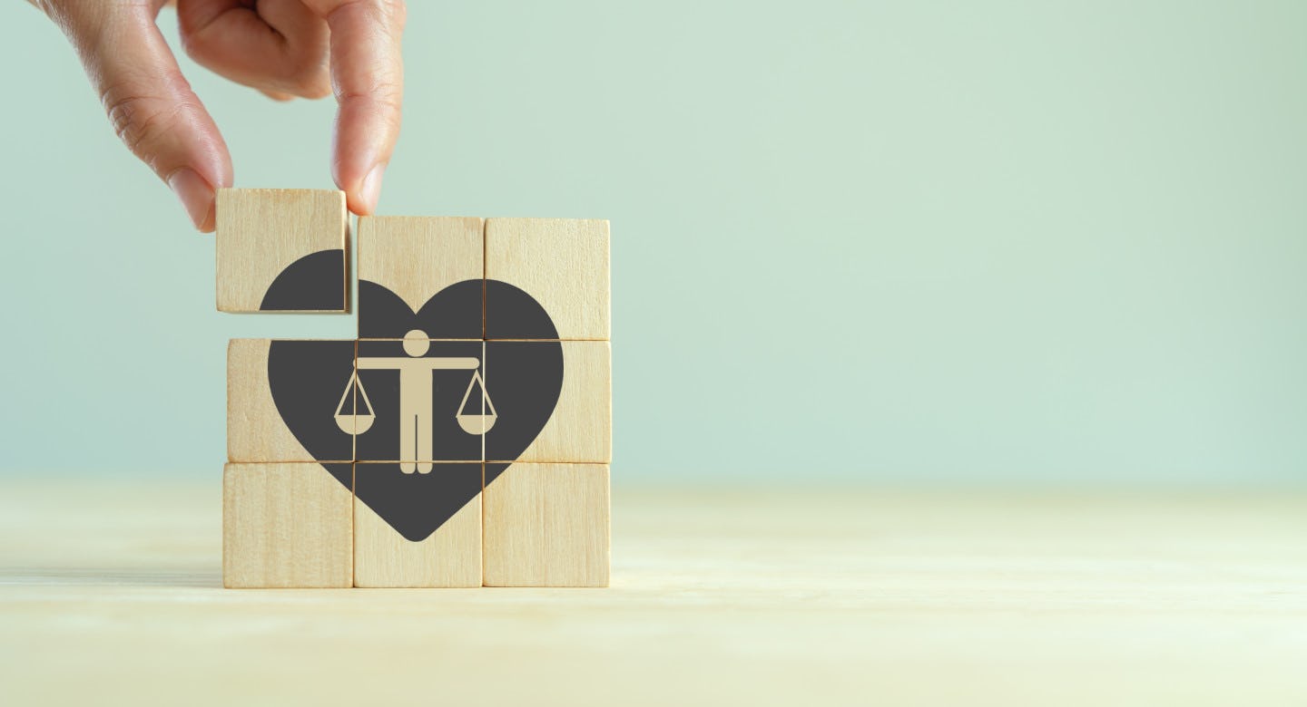 Hand legt houten blokjes met die samen een hart en een figuur met weegschaal vormen als symbool voor ethische belang